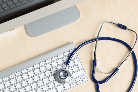 medicine doctor's working table view from top. monitor, keyboard, mouse and stethoscope lying on table at physician's office. medical concept